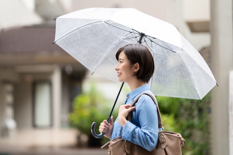 梅雨の中傘をさす笑顔の女性